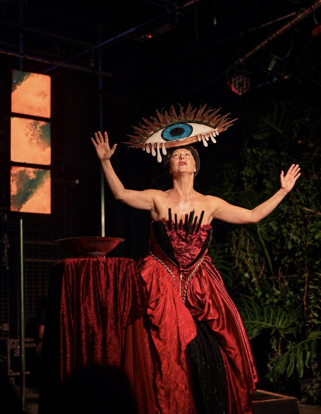 Laura King on stage with arms raised, in the eye headdress and red gown.
